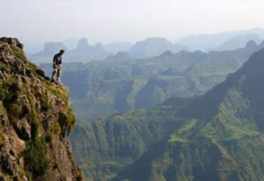 ከገደሉ በላይ በዓለት ጫፍ ላይ የቆመ ተጓዥ